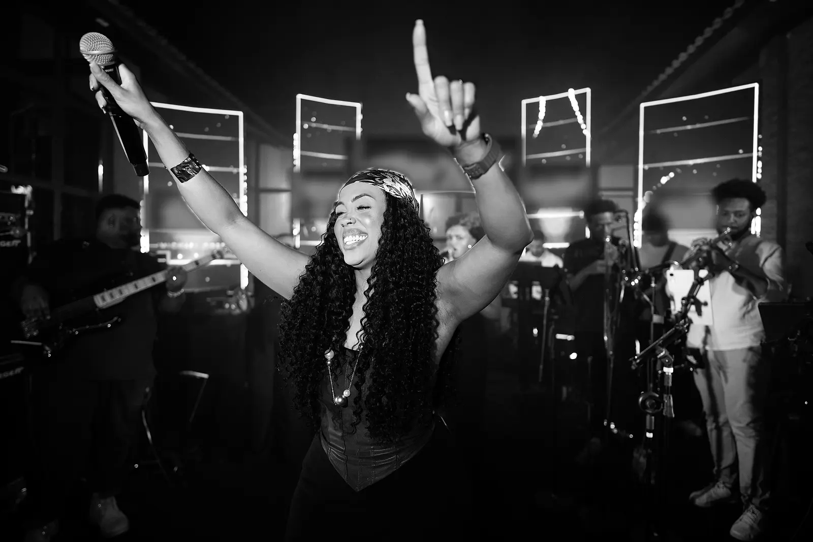 Cantora da Black SP de braços erguidos no palco, com a banda atrás